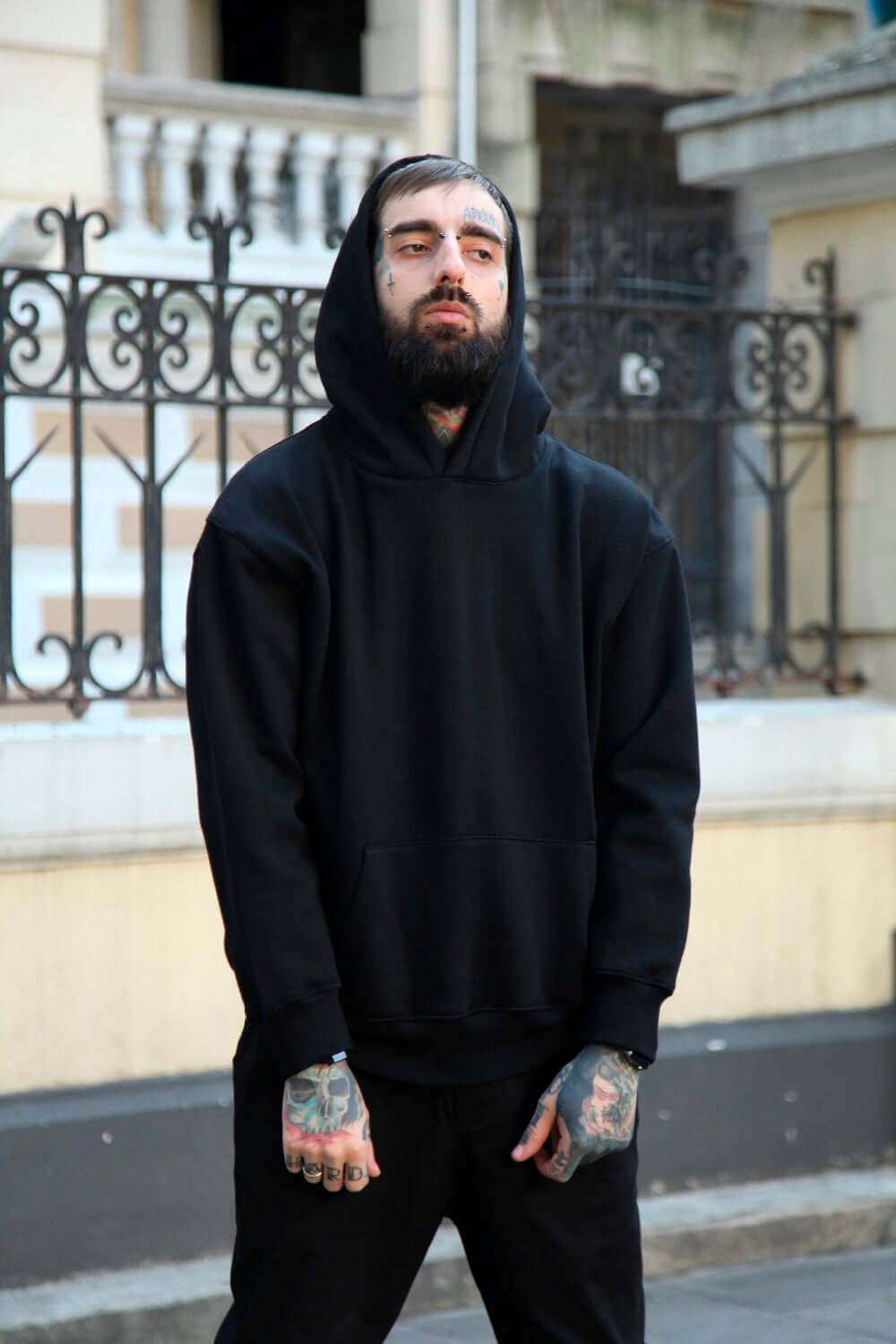 Plain multi colored hoodies worn by a man with tattoos, in a stylish urban setting.